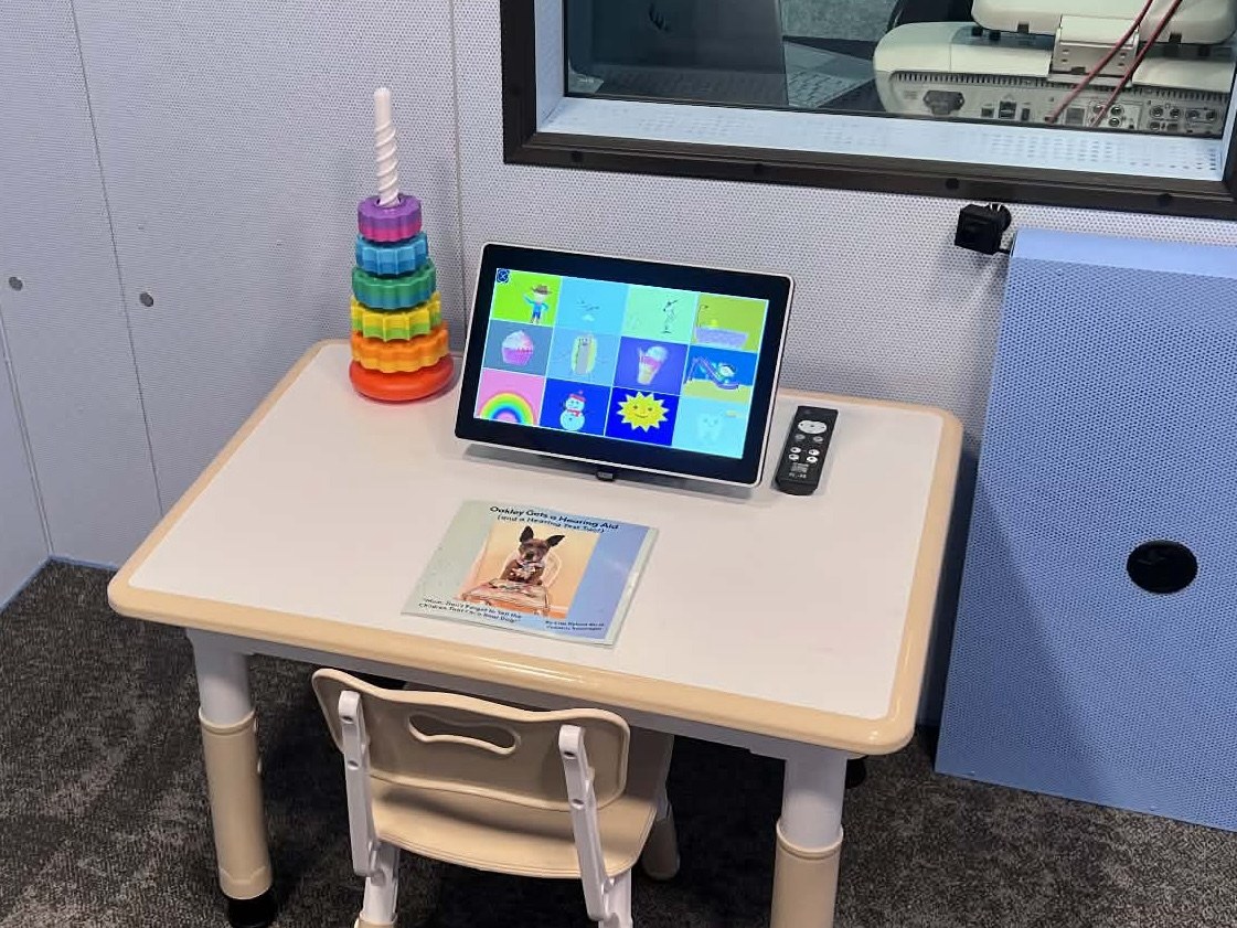 Oakley’s book on a pediatric soundbooth table beside a colorful hearing-test display